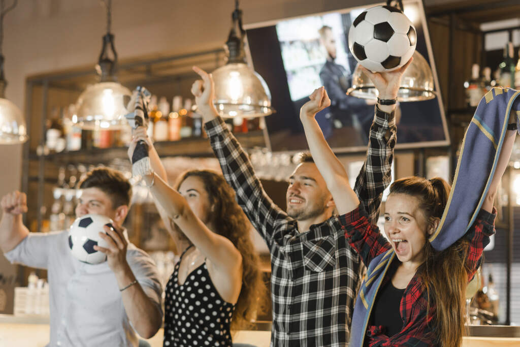 4 pessoas comemorando algo em um bar, segurando bolas de futebol em suas mãos.