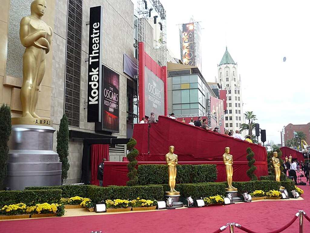 Entrada pelo tapete vermelho para cerimônia de entrega do Oscar, com estatuetas douradas cercando a entrada.