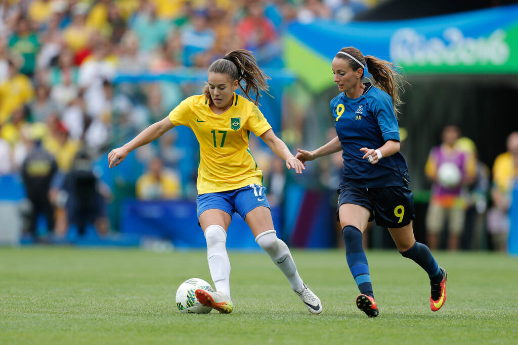 Jogadora de futebol da seleção brasileira conduzindo a bola durante partida entre seleções.