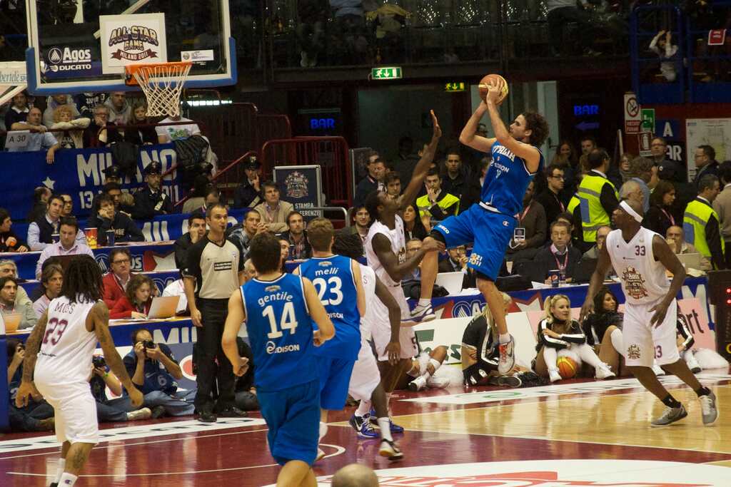 Jogador de basquete vestindo uniforme azul, realizando um arremesso durante partida.