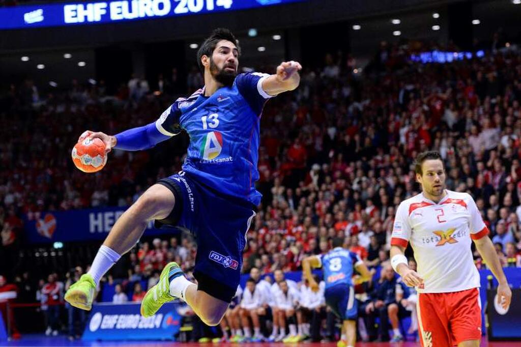 Jogador de handebol vestindo uniforme azul com detalhes amarelos, saltando e realizando arremesso no ar, durante partida.