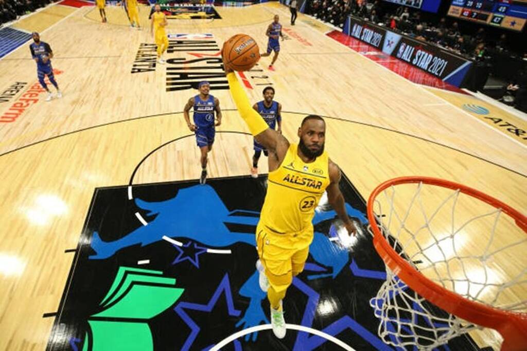 Jogador de basquete vestindo uniforme amarelo e realizando uma enterrada durante partida do All-Star Game.