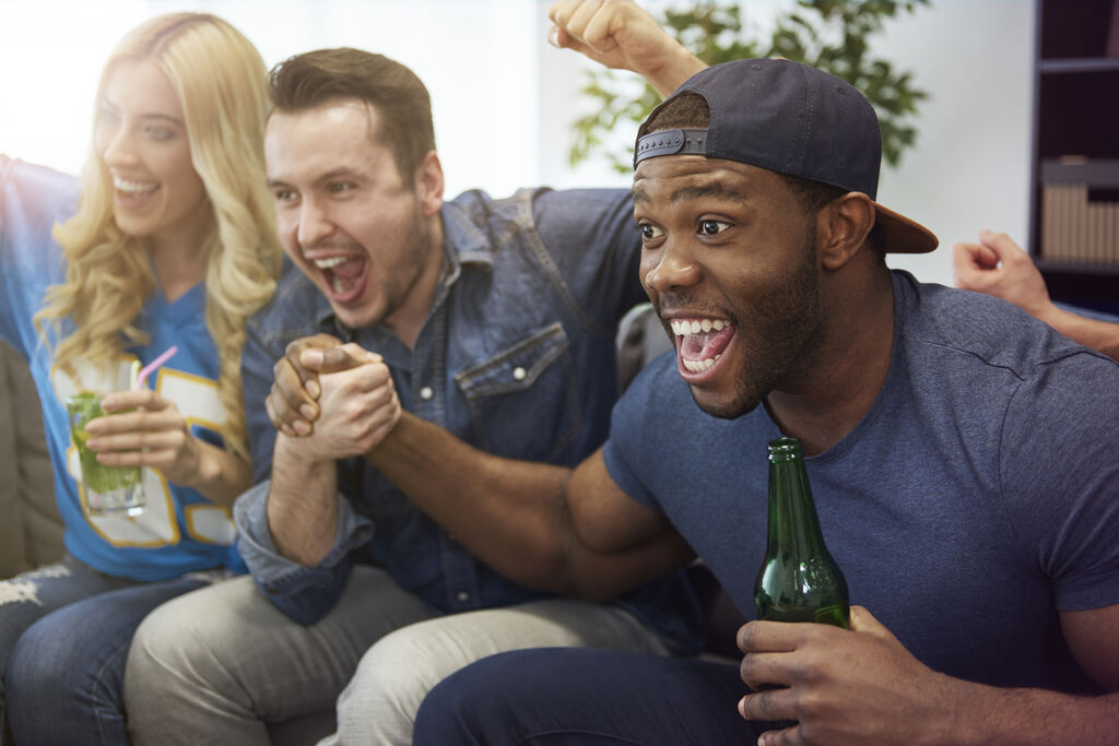 3 pessoas comemorando algo intensamente, sentados em um sofá e tomando cerveja.