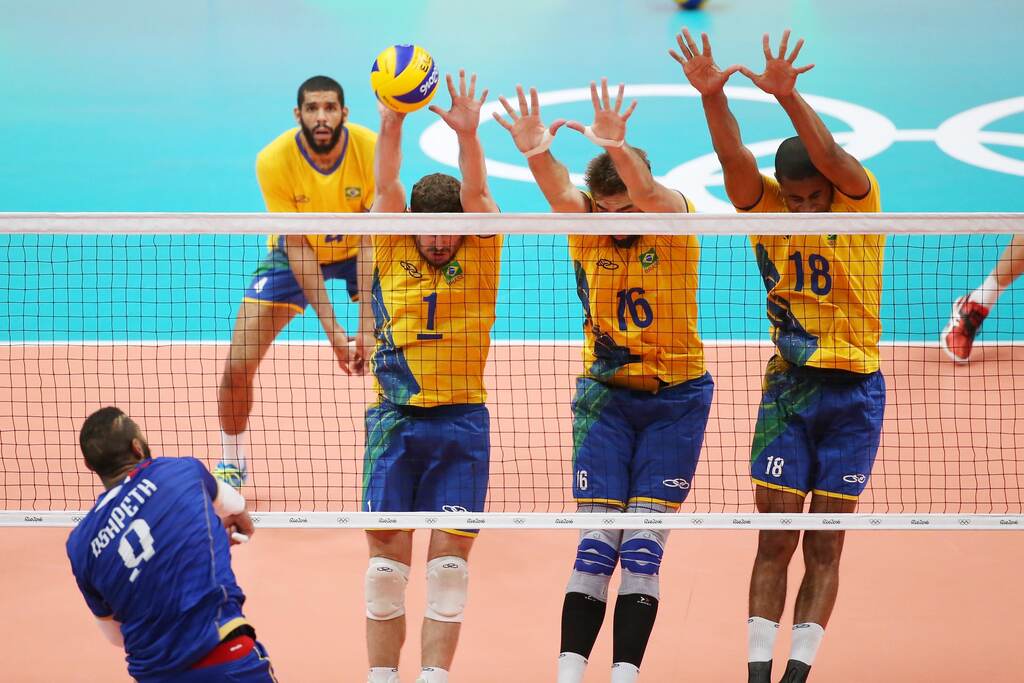 Jogadores da seleção brasileira de vôlei bloqueando cortada de jogador da seleção adversãria.