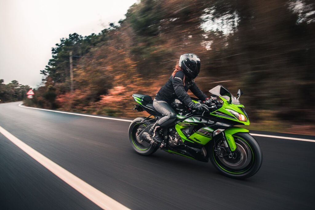 Pessoa dirigindo uma moto preta com detalhes verdes em alta velocidade em uma estrada.