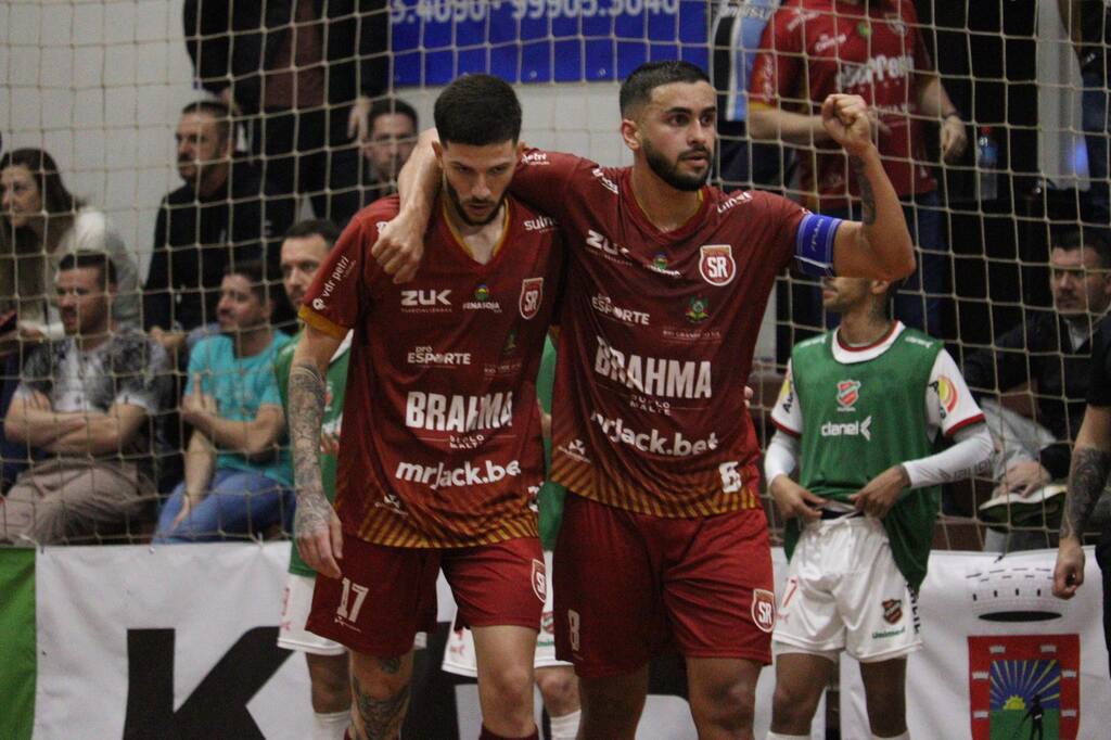 Jogadores de futsal vestindo uniforme bordô abraçados andando pela quadra.