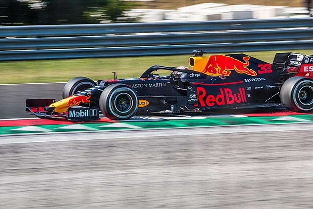 Carro de corrida da Red Bull preto com detalhes vermelhos e laranja, correndo em pista esportiva.