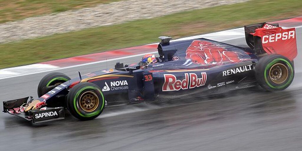 Carro de corrida, preto com detalhes vermelhos, sendo pilotado em pista de corrida de fórmula 1.