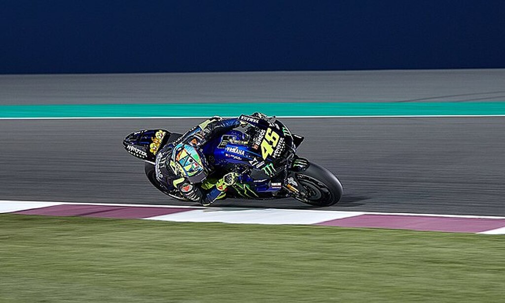 Piloto de corrida de moto fazendo curva em alta velocidade, quase encostando no chão.