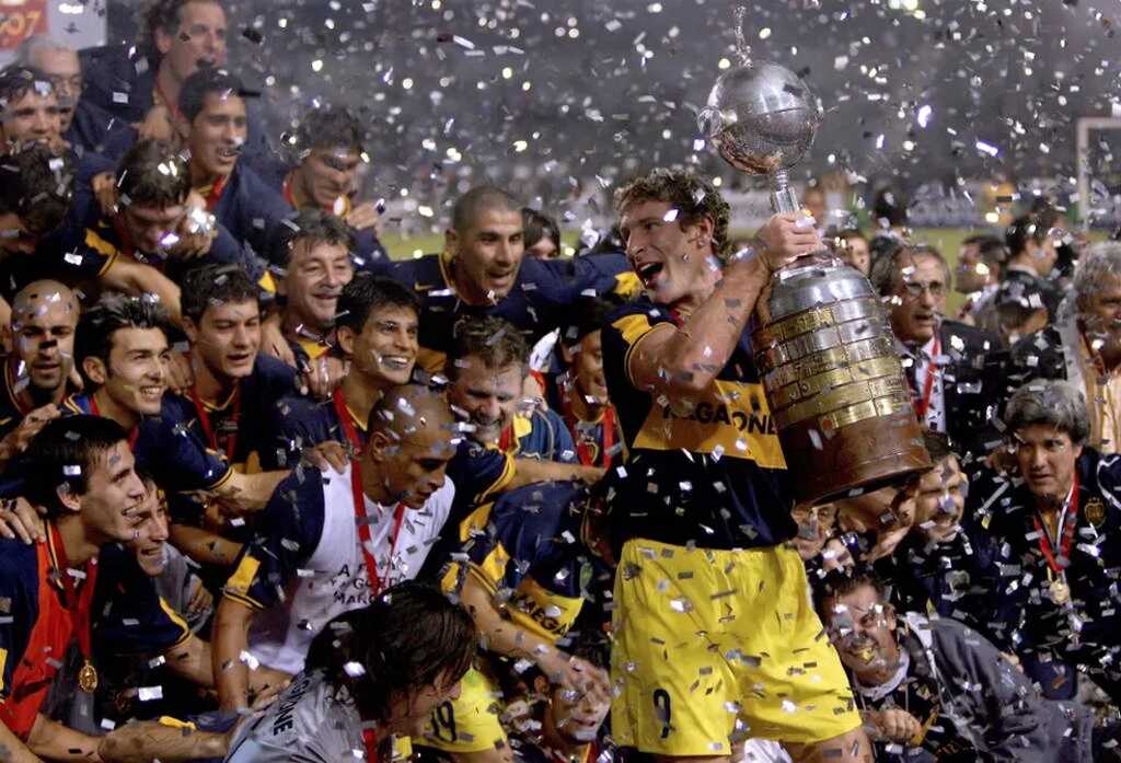 Jogadores do Boca Juniors comemorando título da Libertadores no gramado, com seu capitão erguendo a taça.