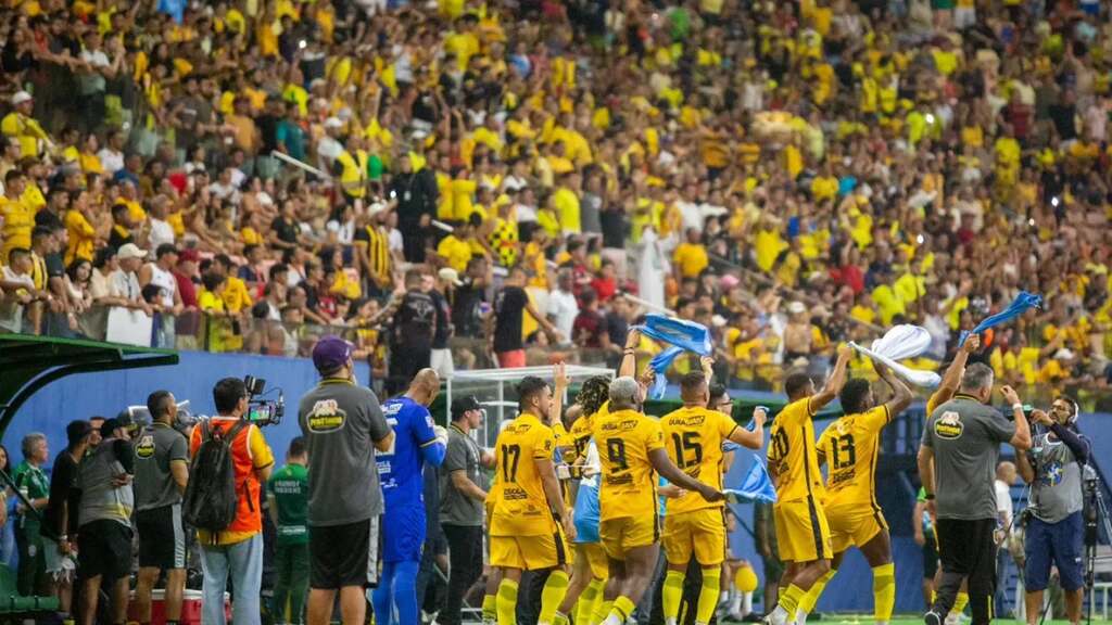 Jogadores do Amazonas FC, vestindo uniforme amarelo com detalhes pretos comemorando com a torcida.