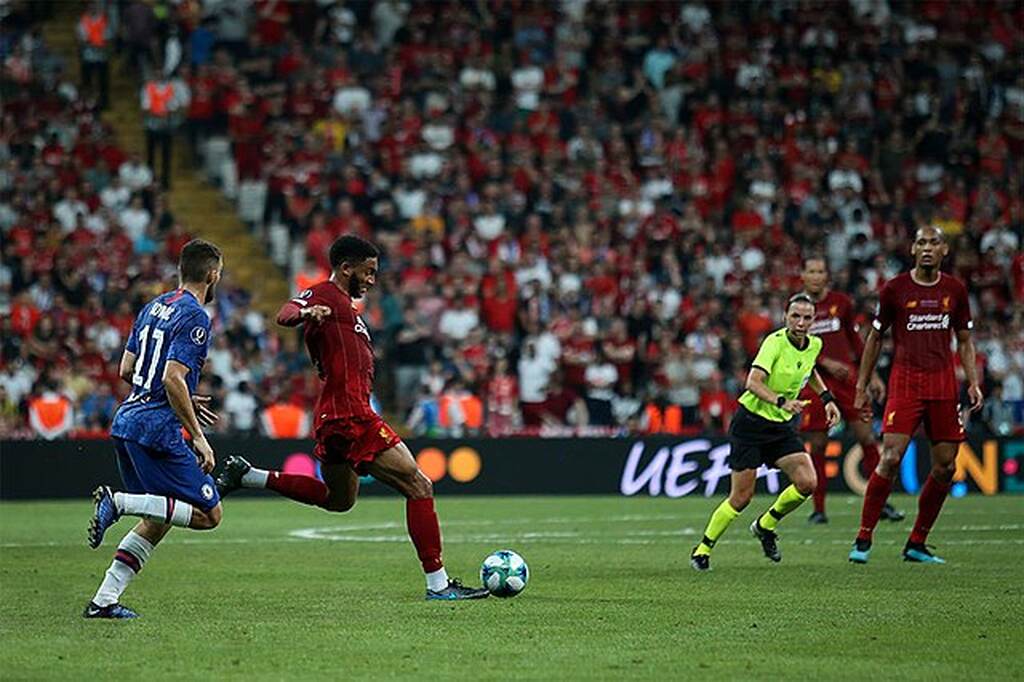 Jogador do Liverpool, com o tradicional uniforme vermelho do clube, chutando a bola durante a partida.