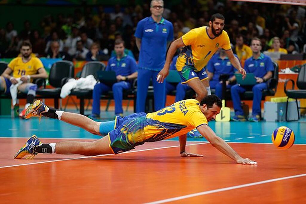 Seleção brasileira de vôlei masculino durante partida. Um jogador se lança ao chão para evitar o ponto do adversário.