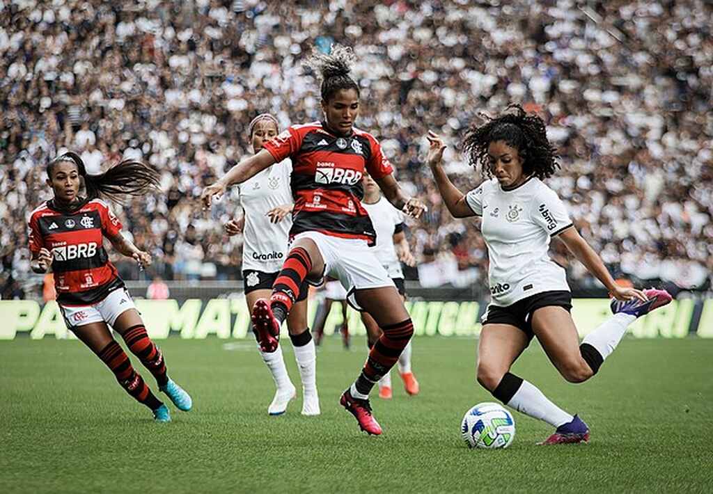 Jogadora do time feminino do Corinthians realizando chute enquanto jogadora do Flamengo tenta bloquear.