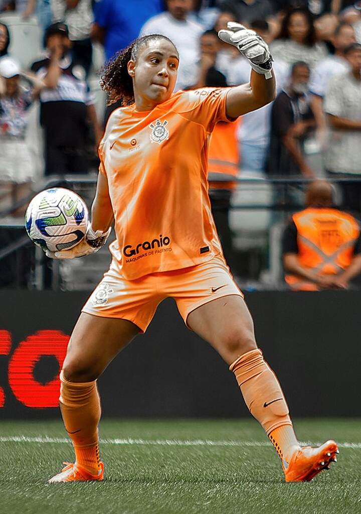 Goleira do time feminino do Corinthians, vestindo uniforme laranja e arremessando a bola de volta ao jogo.