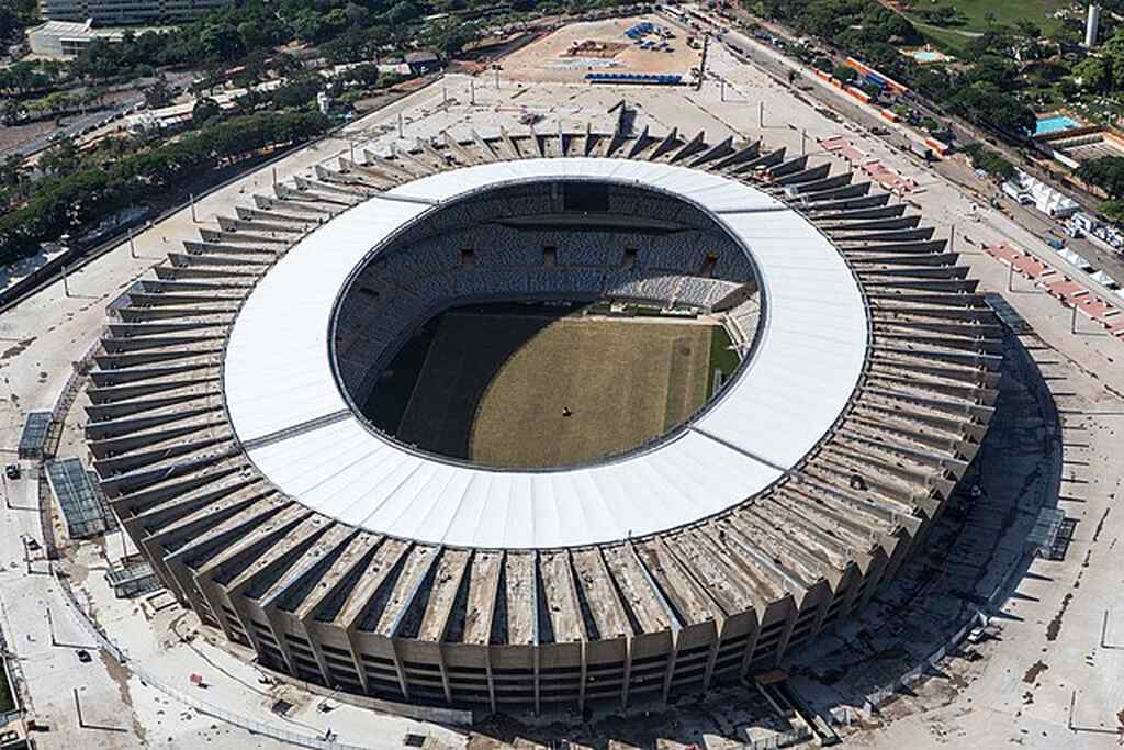 Visão do alto do estádio mineira, com arquibancadas vazias, e estacionamento ao redor.