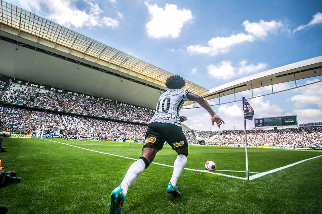 Jogador de futebol Willian, do Corinthians, com calção preto e camisa branca, realizando cobrança de escanteio.