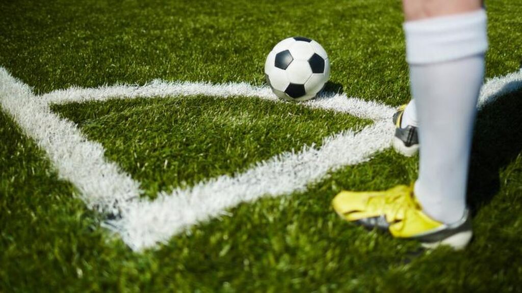 Jogador de futebol vestindo chuteira amarela e meião branco, com a bola de futebol na marca de escanteio, pronto para cobrar.