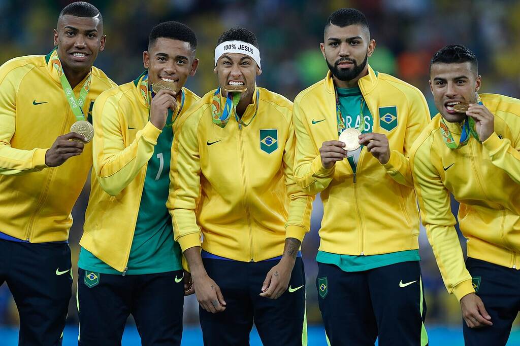 Jogadores da seleção brasileira de futebol, com casacos da seleção, comemorando medalha de ouro das Olimpíadas.