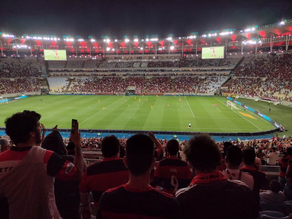 Torcida do Flamengo na arquibancada do Maracanã durante partida de futebol, com o ouro lado do estádio parcialmente vazio. 