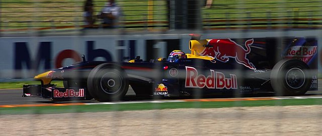 Carro preto com detalhes amarelos e vermelhos, da Red Bull, durante corrida de Fórmula 1.