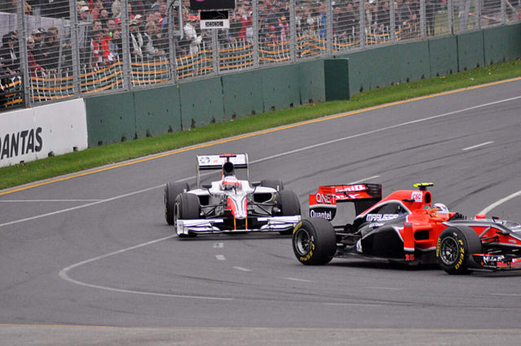 Carro branco com detalhes vermelhos tentando ultrapassar carro vermelho durante curva em corrida de Fórmula 1.