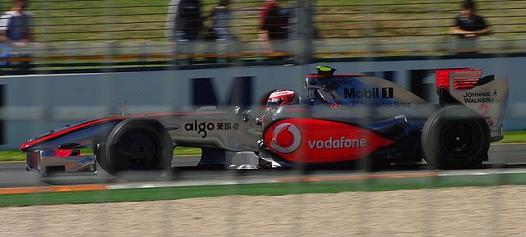 Carro cinza com detalhes vermelhos, realizando curva durante corrida de Fórmula 1.