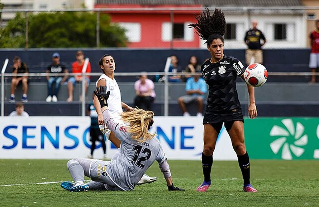 Jogadora co Corinthians feminino, de uniforme preto, dividindo bola com goleira do time adversário vestida de uniforme cinza.