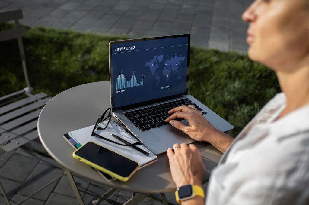 Homem de camisa branca, usando um notebook cinza com gráficos e informações de países na tela.