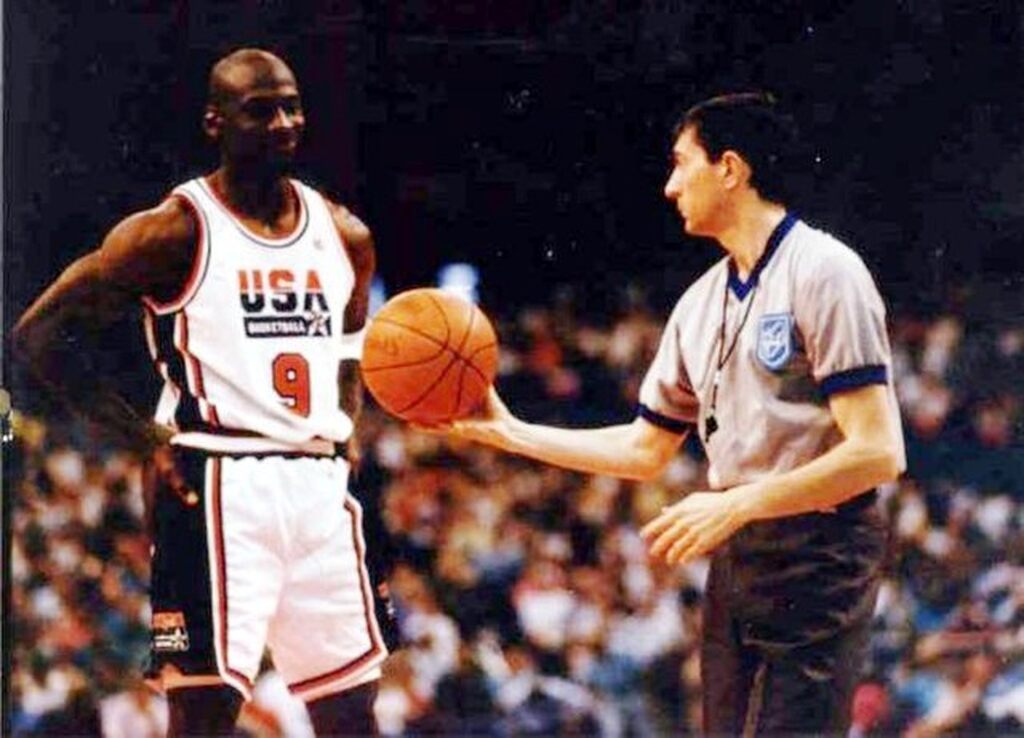 Árbitro de basquete segurando uma bola laranja e entregando ela para o Michael Jordan durante partida.