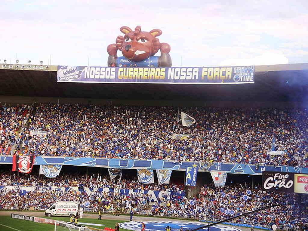 Vista da arquibancada do estádio lotado, com torcida do Cruzeiro erguendo boneco inflável da raposa.