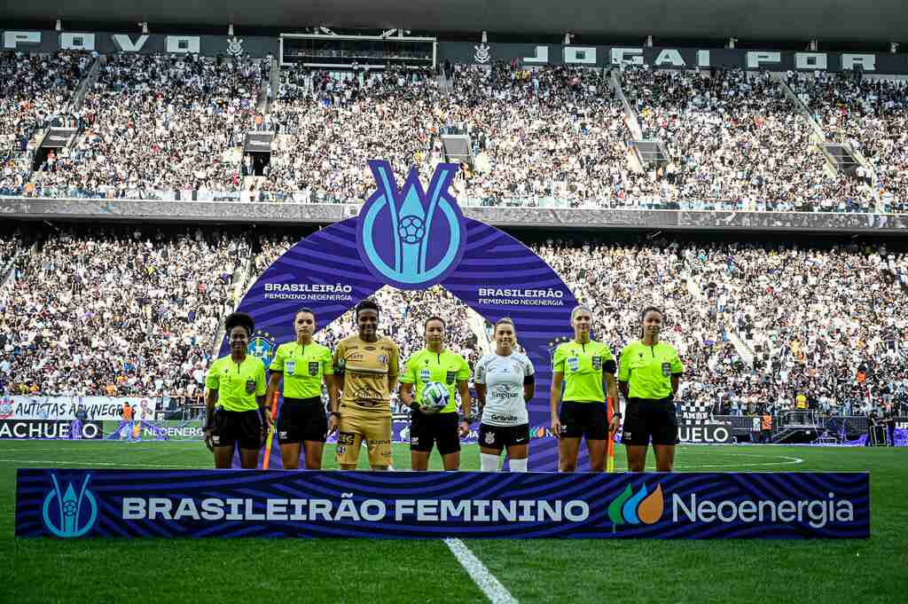 Equipe de arbitragem e jogadores de Ferroviária e Corinthians posando perfiladas atras de um letreiro do Brasileirão Feminino 2023