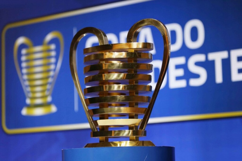 Taça da Copa do Nordeste exposta em frente a uma faixa com o logo do campeonato.