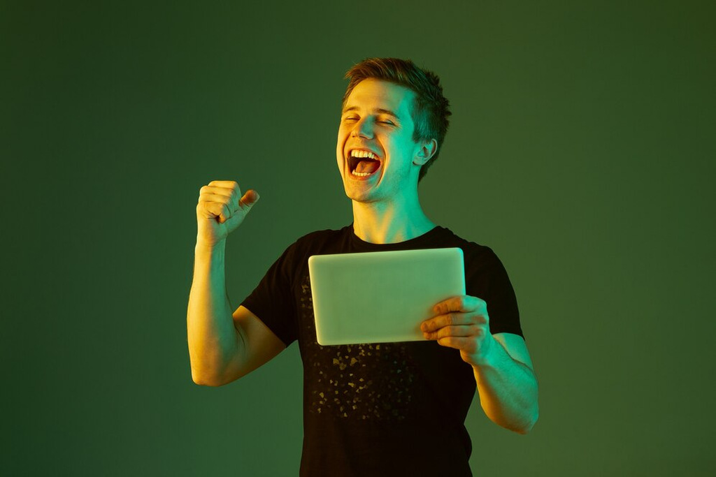 homem que representa um dos perfis de apostadores do brasil segurando um tablet enquanto comemora o green da aposta