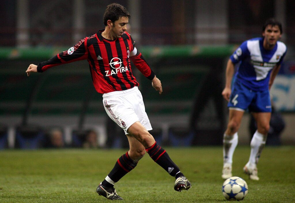 Ex-jogador de futebol do Milan, Alessandro Costacurta, vestindo uniforme vermelho com listras pretas e realizando passe.