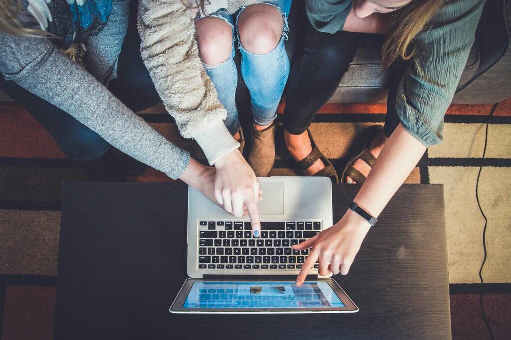 3 pessoas sentadas, com um notebook colocado sobre a mesa e as 3 apontando para algo em sua tela.