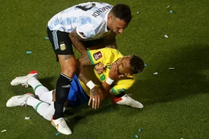 Jogador do brasil caido com um jogador da argentina tentando levanta-lo 