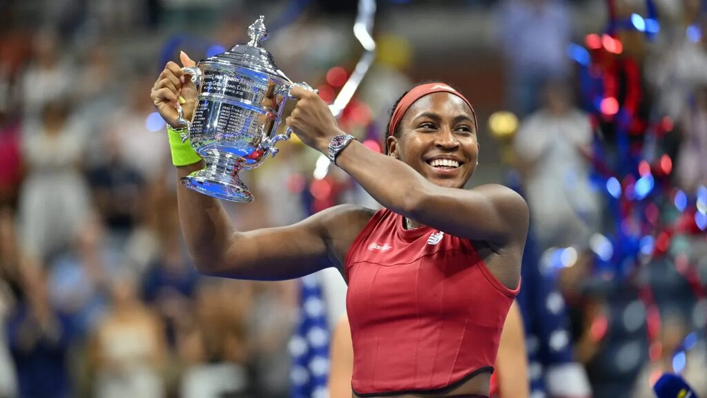 Jogadora de tênis Coco Gauff, vestindo uniforme vermelho, segurando troféu prateado com as duas mãos.