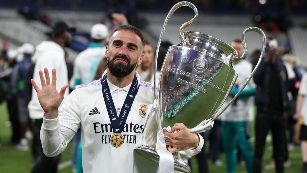 Jogador de futebol do Real Madrid, Carvajal, vestindo uniforme branco do clube enquanto segura a taça de campeão.