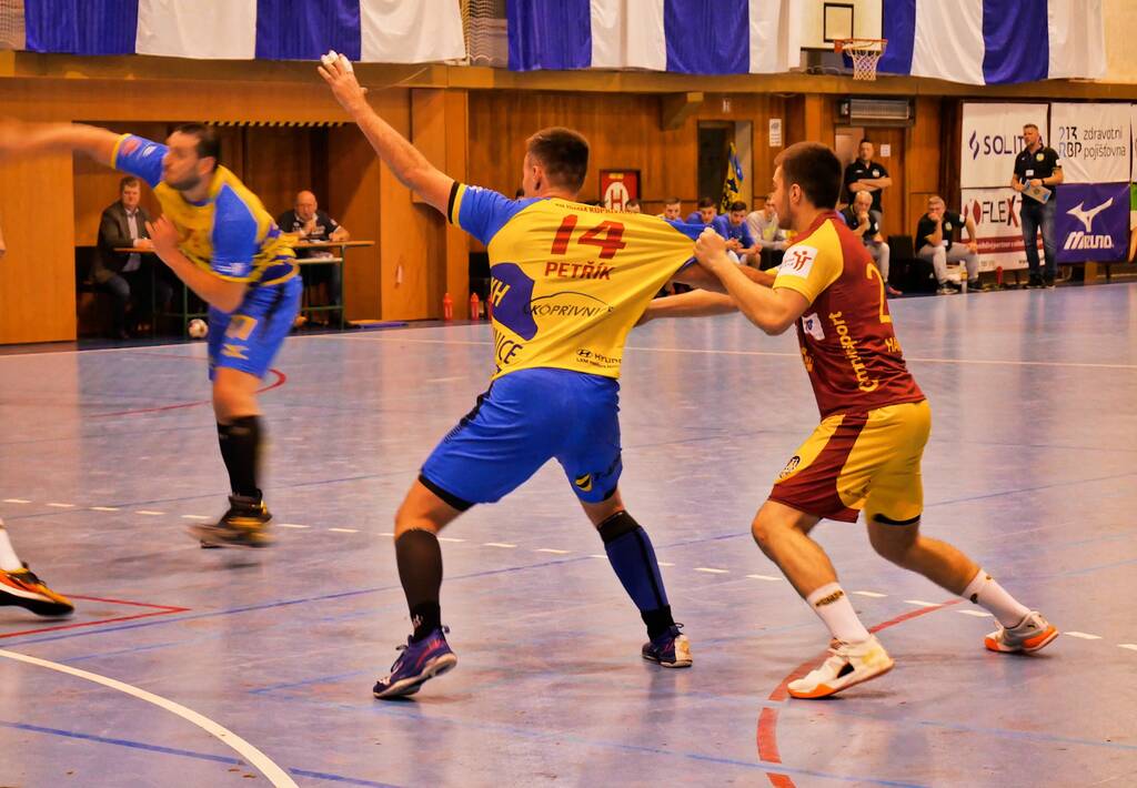 Jogador de handebol de uniforme amarelo com detalhes azuis tendo sua camisa puxada pelo adversário.