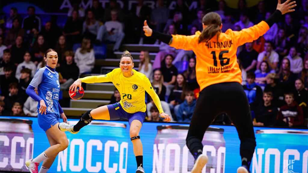 Jogadora de handebol, vestindo uniforme amarelo, realizando arremesso durante a partida.