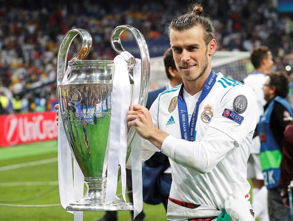 Ex-jogador do Real Madrid, Gareth Bale, segurando a taça de campeão da Champions League e sorrindo.