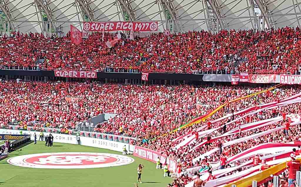 Torcida do Internacional em arquibancada de estádio lotado durante partida de futbol.