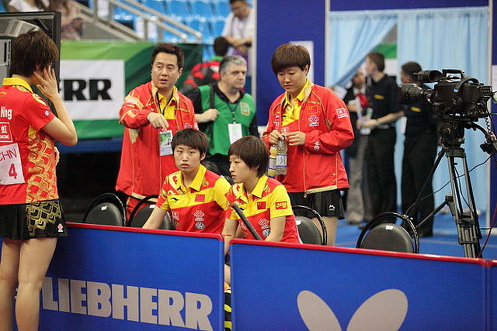 Jogadora da seleção feminina de tênis de mesa da China, vestindo uniformes vermelhos e amarelos durante competição.