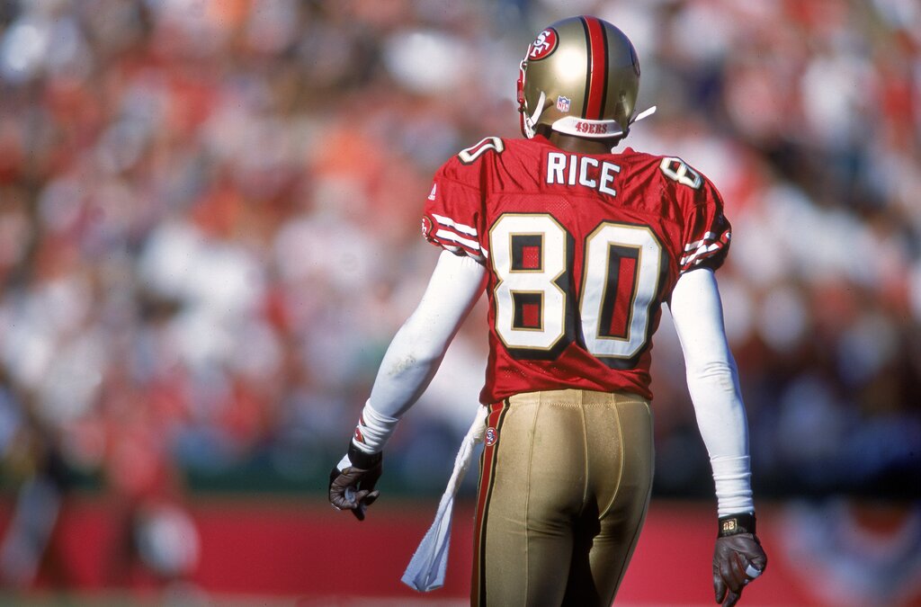 Ex- jogador de futebol americano, Jerry Rice, vestindo uniforme vermelho com detalhes brancos durante partida.