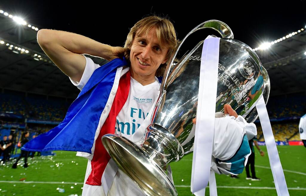 Jogador do Real Madrid Luka Modrić, segurando a taça da Champions League enquanto anda pelo gramado.