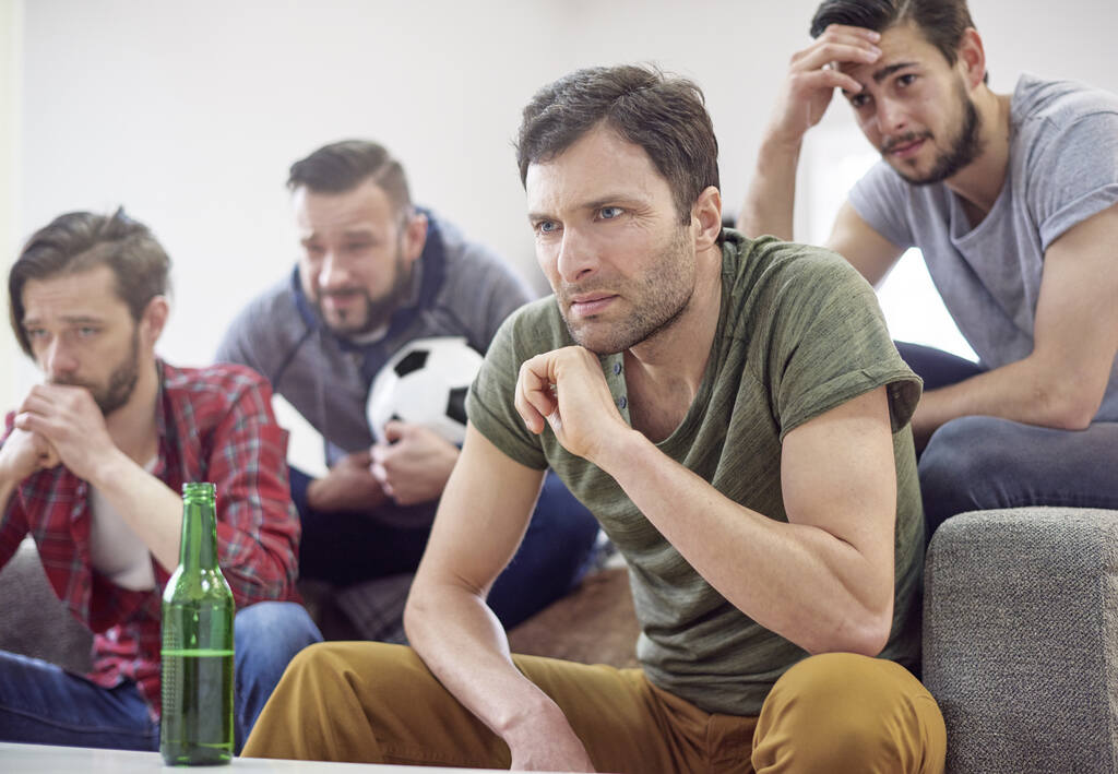 Homens pensativos enquanto assistem à partida de futebol.