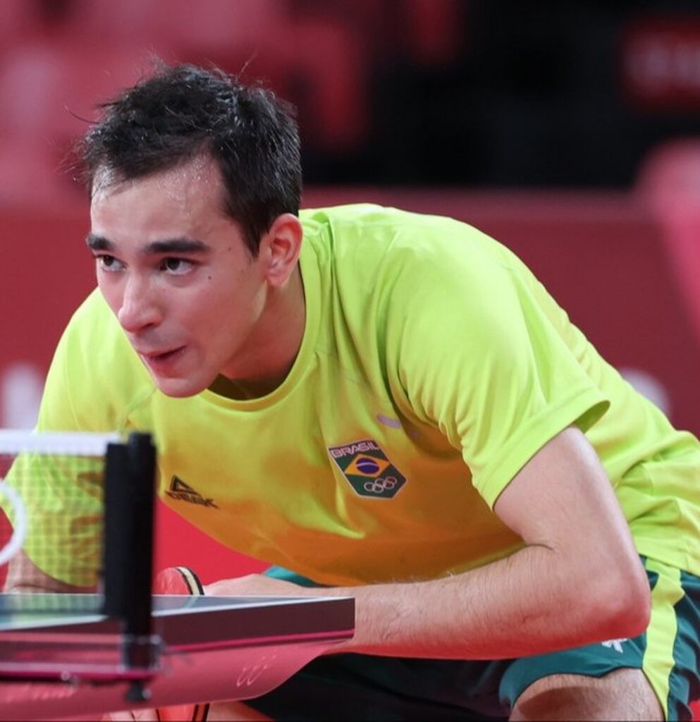 Jogador brasileiro de tênis de mesa, Hugo Calderano, vestindo uniforme amarelo durante partida profissional.