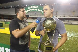 Pessoa sendo entrevistada por um repórter com uma taça de campeão em mãos 