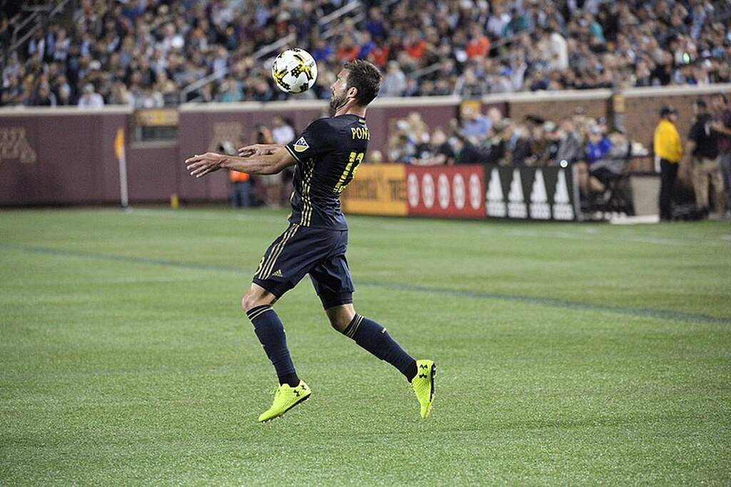 Jogador de futebol da MLS, vestindo uniforme preto, dominando a bola no peito durante a partida.